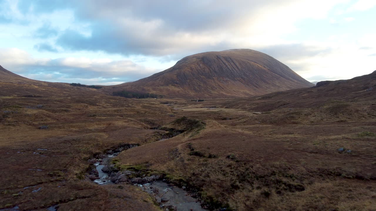 toma aérea de bajo nivel en movimiento lento en la corriente inferior del valle de las colinas y montañas en glencoe, escocia en gran bretaña