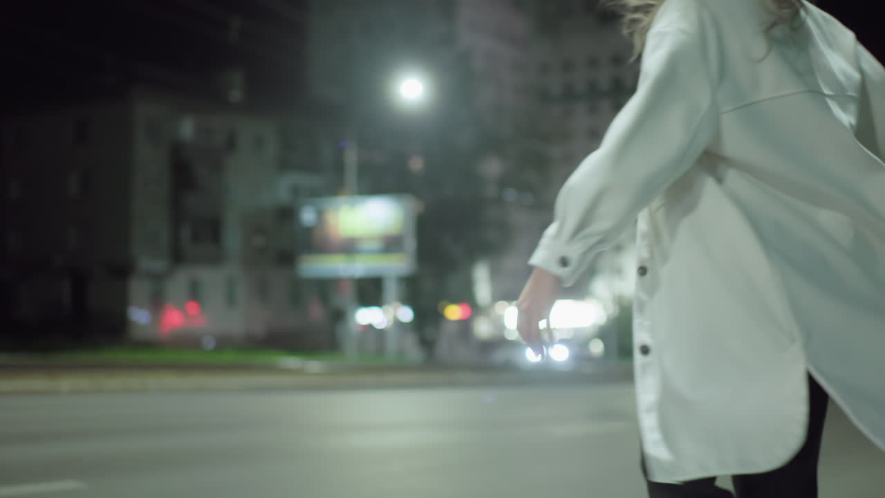 White woman radiates happiness under street light with her face glowing as she smiles joyfully while vehicles pass by and residential buildings blur into colorful nighttime background