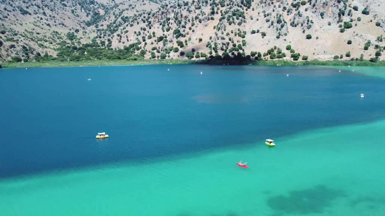 Beautiful Kournas lake in Crete with boats on the turquoise water revealing the mountains and blue sky