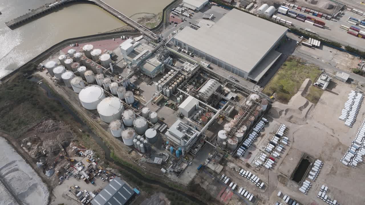 Aerial perspective of riverside tank farm of cylindrical oil storage silos, pipelines and service roads supporting energy distribution along a major waterway