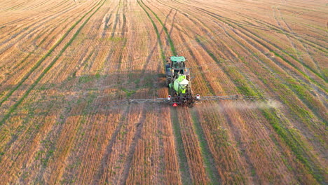 Cinematic-establishing-shot-of-industrial-tractor-spraying-fertilizer-on-farm-field-during-golden-sunset---following-drone-shot