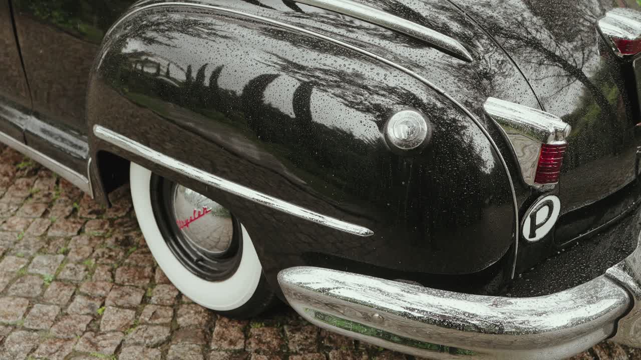 rain covered retro black car showing chrome bumper and whitewall wheel