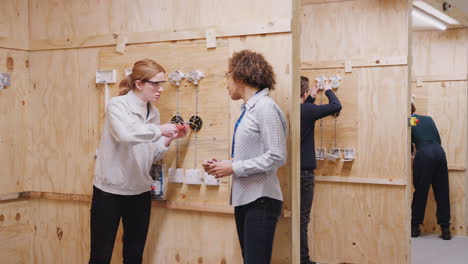 female tutor with trainee electricians in workshop studying for apprenticeship at college