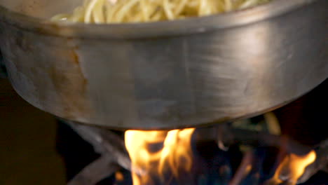 un primer plano de la pasta y las verduras que se cocinan en una sartén sobre el fuego en cámara lenta