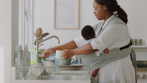 Madre-Afroamericana-Sosteniendo-A-Un-Bebé-Trabajando-En-Casa-Lavando-Platos-Limpiando-La-Cocina-Cuidando-A-Un-Niño-Pequeño-Haciendo-Tareas-Domésticas-Disfrutando-De-La-Maternidad