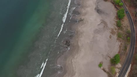 Playa-En-Costa-Rica-Con-Olas-Suaves-Golpeando-Rocas-Y-Creando-Remolinos-Redondos-Cerca-De-La-Carretera,-Toma-De-Rotación-De-Vista-Aérea-Superior