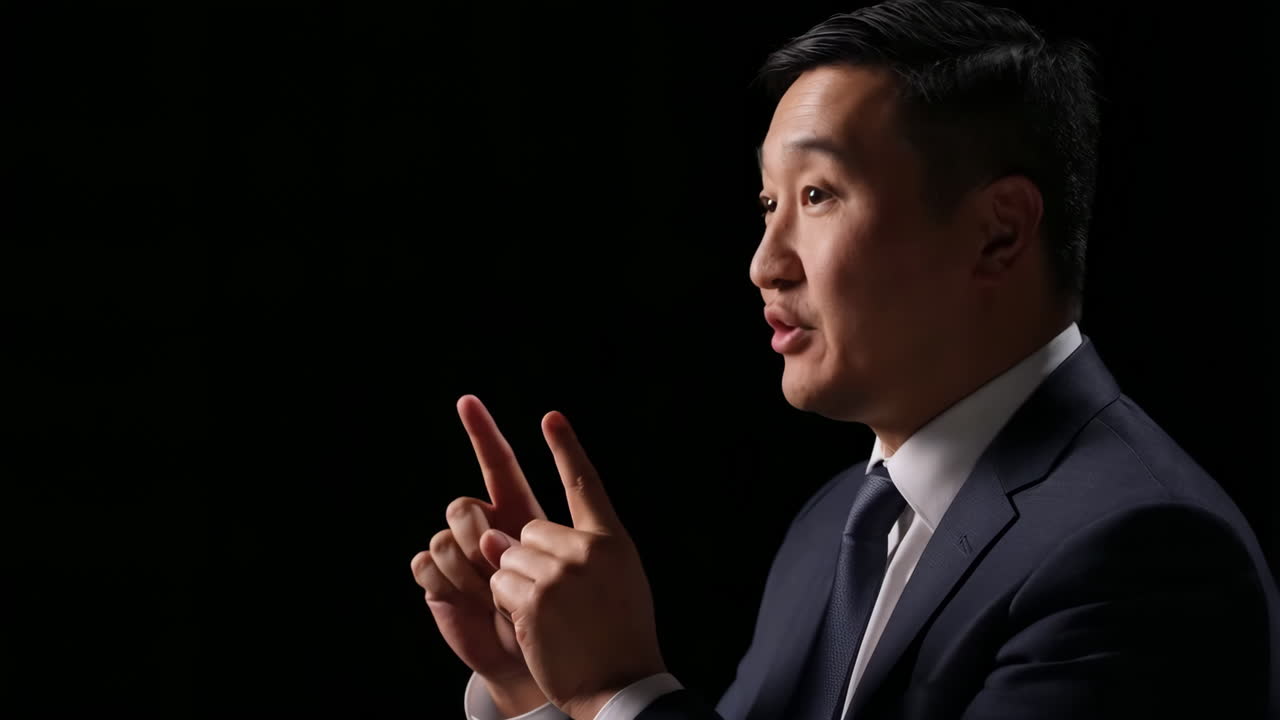 A man in a suit speaking and gesturing against a dark background