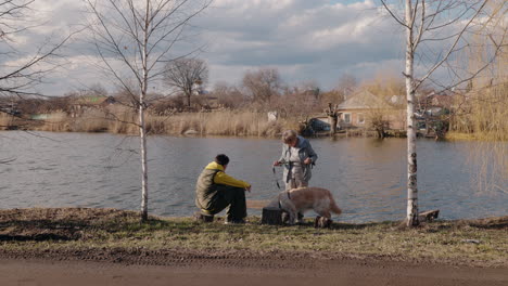 elderly woman and a young man walking with a dog near a riverbank