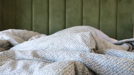 a close-up shot of a bed with white sheets and a green velvet headboard