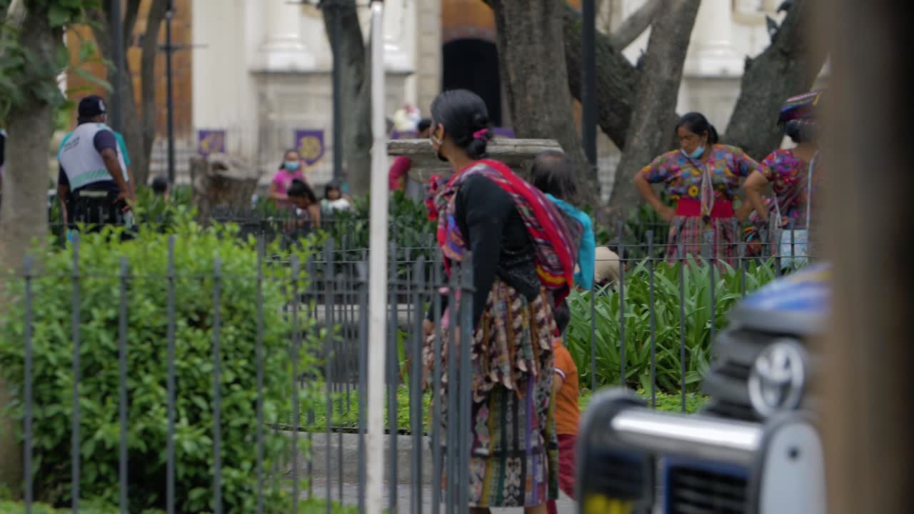 Antigua Guatemala, Sacatepequez Indigenous woman with face mask walks with baby on her back as a police car drives by in front of her - handheld slow motion