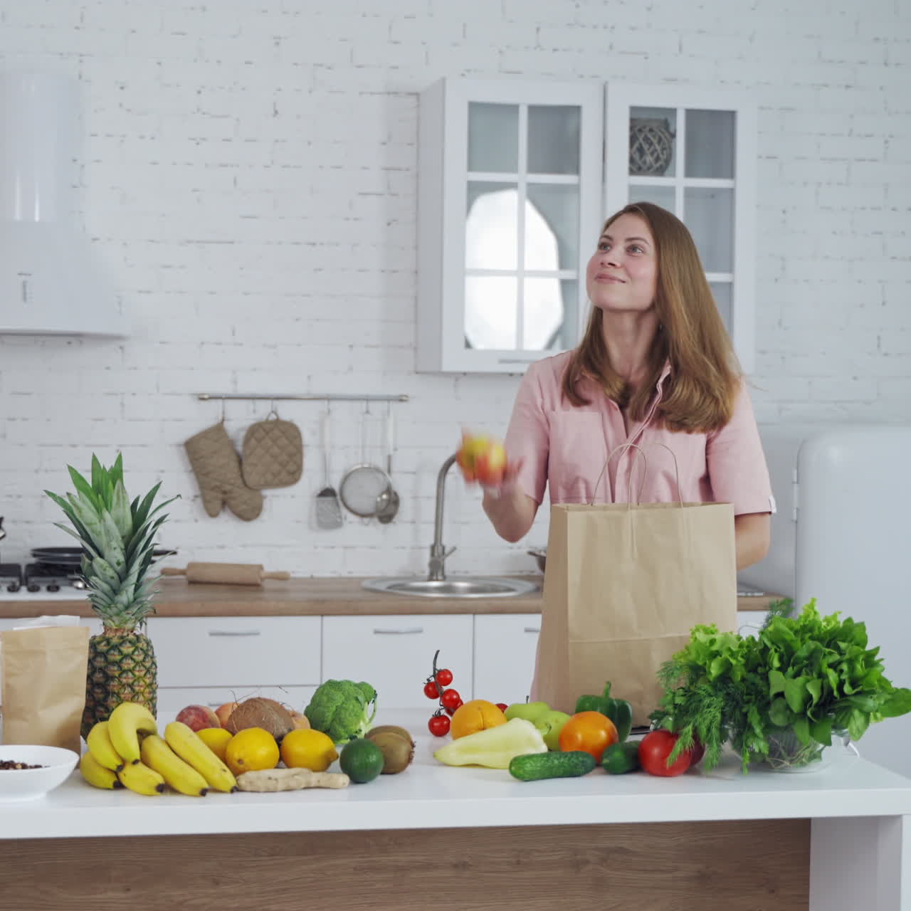 Healthy food on a kitchen table. Beautiful woman taking out fresh apples from shopping bag. Loving mom cares about nutrition.