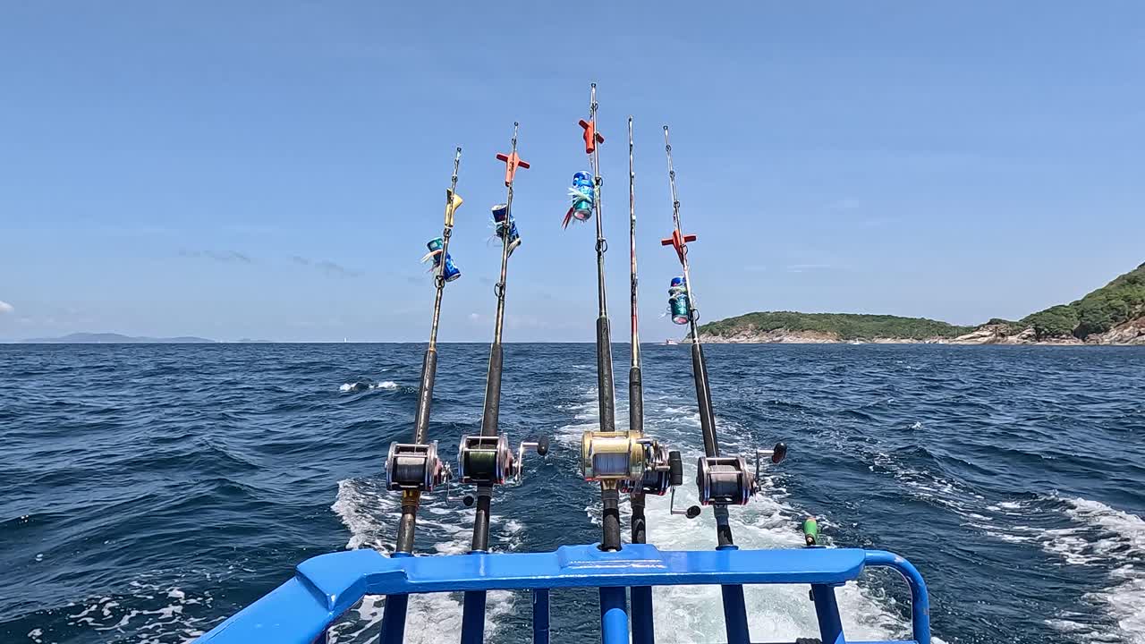 A fishing boat navigates Phuket's ocean, showcasing fishing rods and scenic island views under clear skies