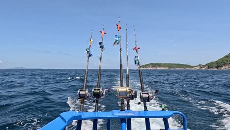 a fishing boat navigates phuket's ocean, showcasing fishing rods and scenic island views under clear skies