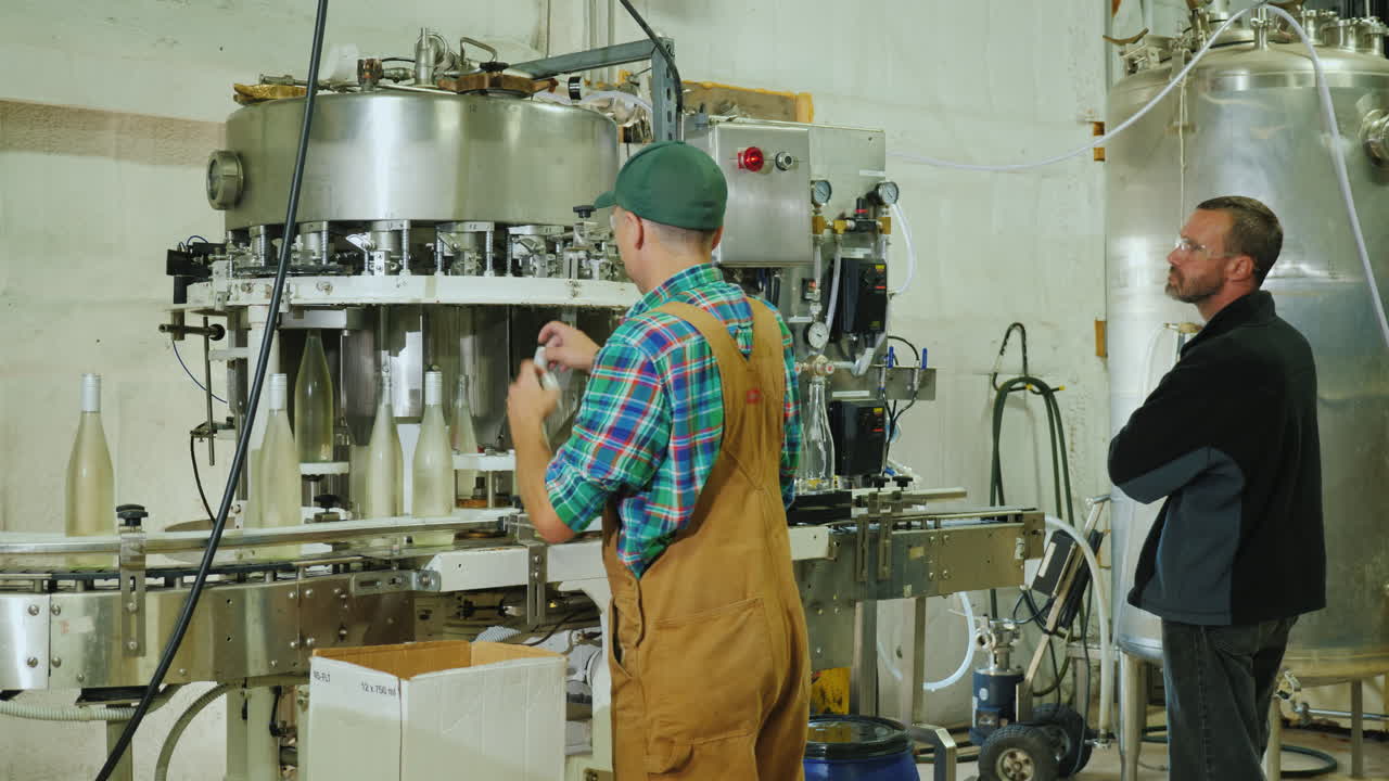 dos trabajadores que trabajan en el transportador donde el vino espumoso embotellado trabaja en una pequeña bodega