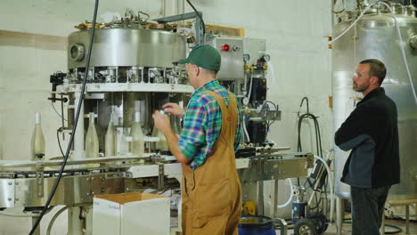 two workers working at the conveyor where bottled sparkling wine work in a small winery