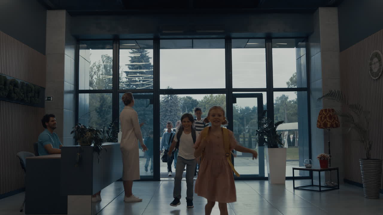 십대 어린이 그룹이 학교 건물에 들어갑니다. 웃는 선생님이 학생들을 환영합니다.