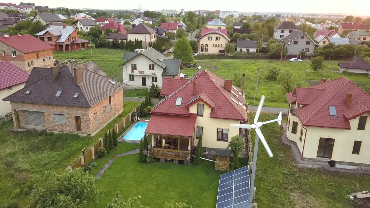воздушный вид на пригородные дома и частный дом с зеленым травяным двором, солнечными панелями на крыше, бассейном с голубой водой и ветряным турбиновым генератором.