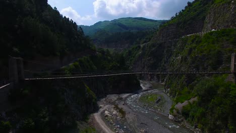 Wooden-bridge-at-river,-and-mountains-in-Kashmir,-India,-Dry-river-going-through-mountains,-Green-Hills-and-mountains-filled-with-trees-and-forest