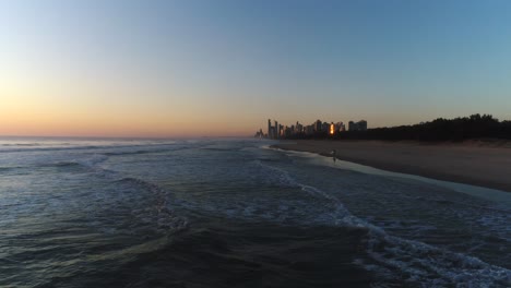 aerial view of a beautiful sunrise lighting up the city of surface paradise in the background with a surfer entering the water to catch some waves at southport gold coast qld australia