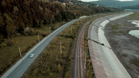 Aerial-shot-of-silver-car-driving-along-the-railway-and-dry-lake