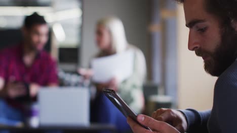 Diverse-business-people-sitting-using-digital-tablet-and-goign-through-paperwork-in-modern-office