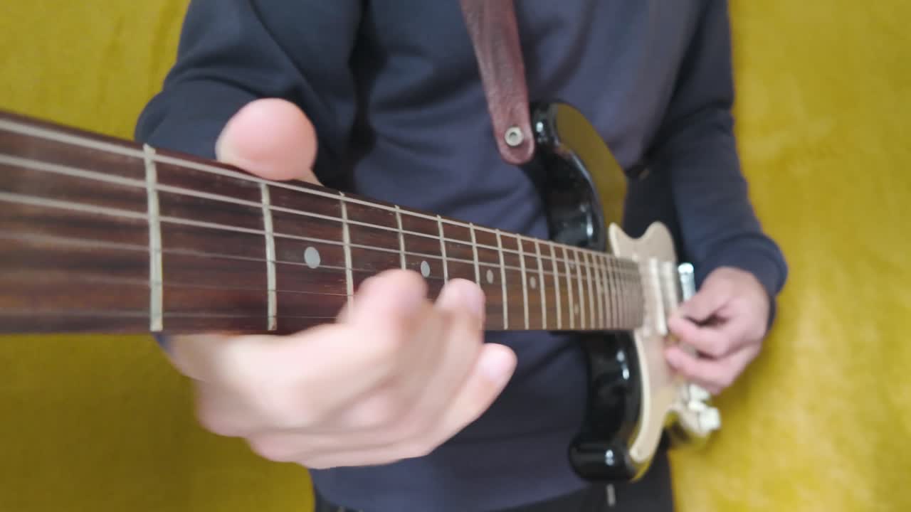 Close up of a hand playing an electric guitar in slow motion against a yellow background