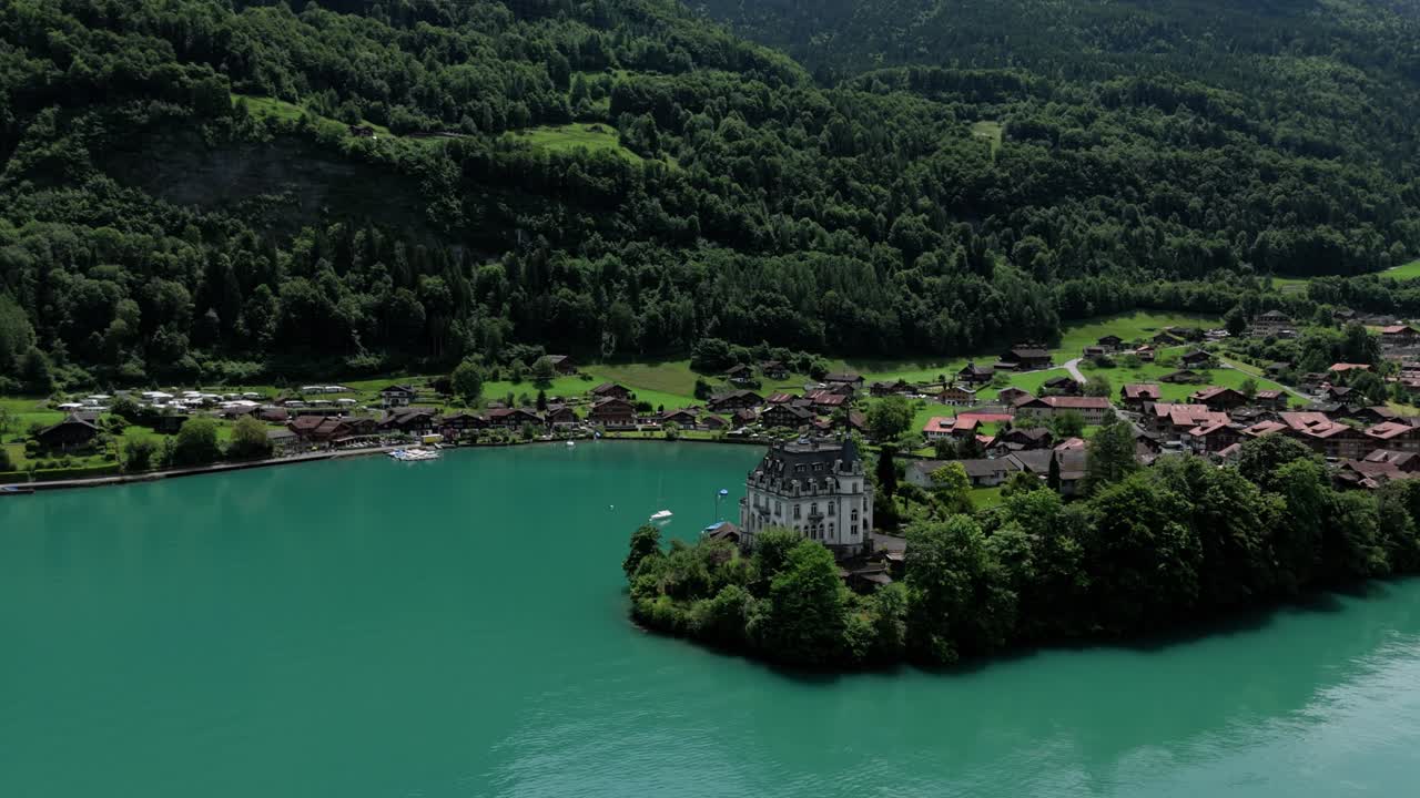 Aerial orbit arround castle Seeburg revealing the view of the turquoise lake Brienzersee Iseltwald surrounded by the alpmointains on a sunny summer day in Switzerland near Interlaken