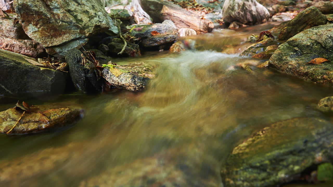 Babbling brook flowing along a rocky creek bed in autumn - long exposure time lapse