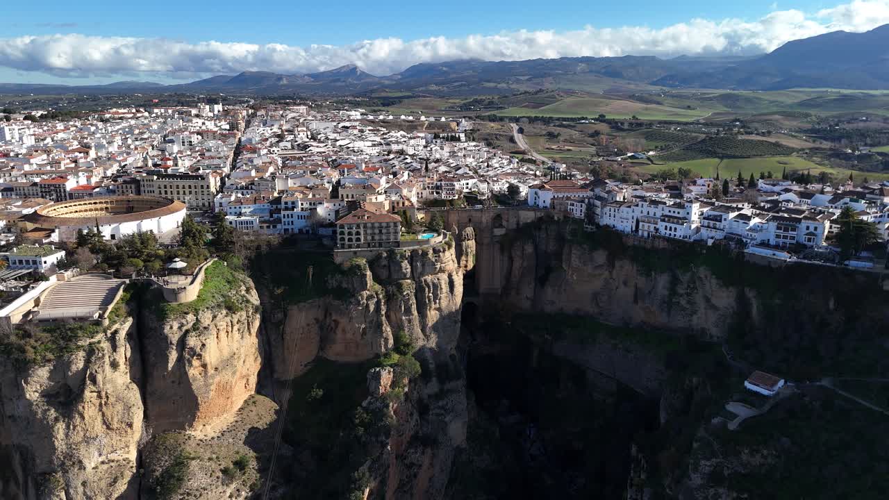 Ronda, Spain, showcases its stunning cityscape perched atop dramatic cliffs, with white buildings contrasting against the rugged terrain under a vibrant blue sky