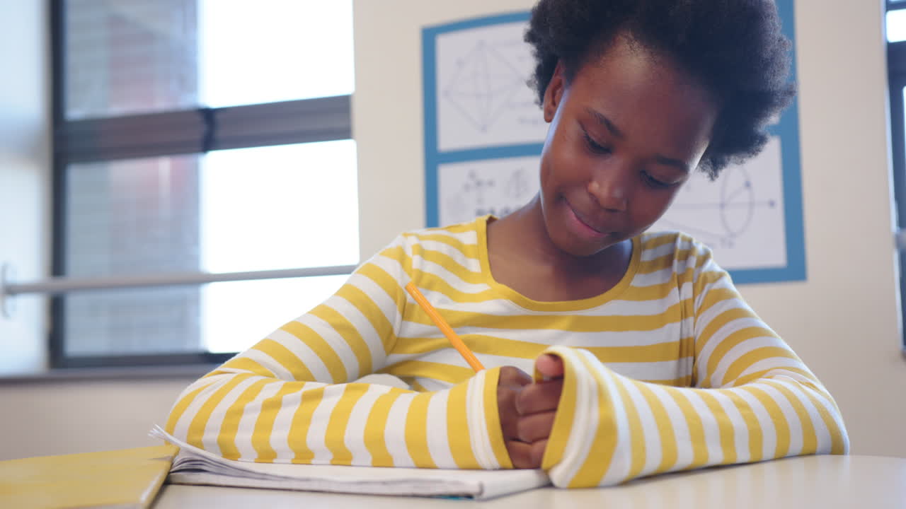 À l'école, une fille tenant un crayon et écrivant dans un cahier, souriant dans une salle de classe.