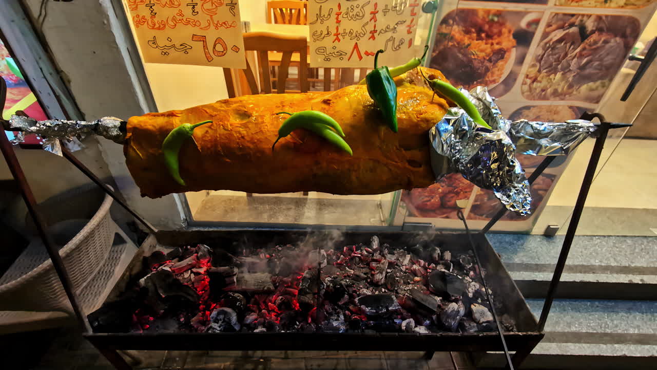 Large shawarma wrapped in foil and topped with green chilies turns on a spit over hot coals. Egypt