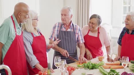 happy group of diverse senior male and female friends preparing food talking in kitchen, slow motion