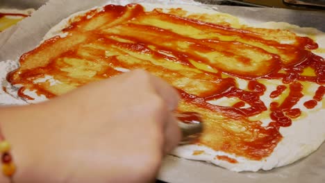 female home cook is spreading tomato ketchup and olive oil on the freshly made pizza dough