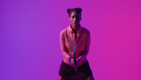 Video-of-focused-african-american-female-tennis-player-with-racket-in-neon-pink-lightning