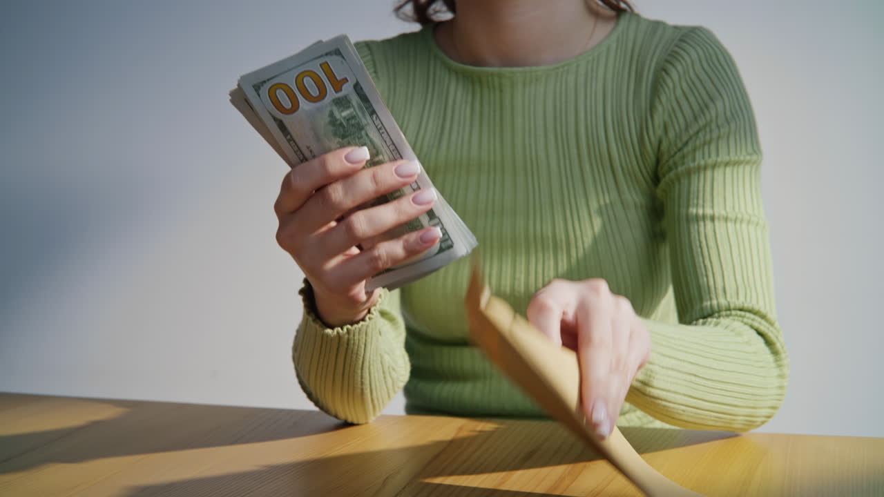 Primo piano di mani femminili che tengono un pacco di dollari. Donna che mette banconote dentro una busta
