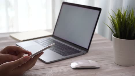mujer joven trabajando desde casa usando teléfono inteligente y computadora portátil en la mesa, las manos de la mujer usando tecnología de teléfono inteligente,