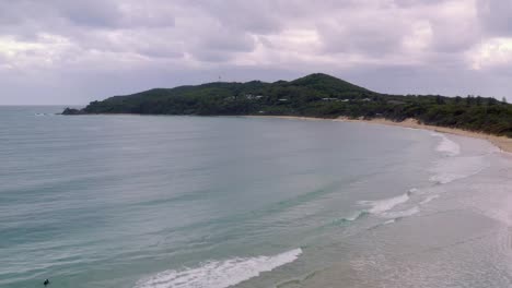 Agua-Azul-Clara-Bajo-Un-Cielo-Nublado-Con-Un-Exuberante-Paisaje-Verde-Ciudad-Costera-En-Byron-Bay,-Australia