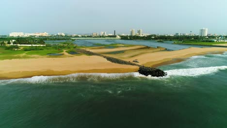 Drone-footage-of-Beach-with-a-backwater-opening-to-it-with-a-city-skyline-with-high-rises-in-backdrop