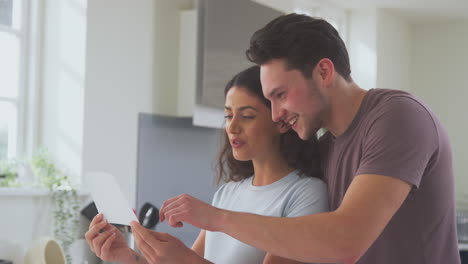 excited pregnant transgender couple at home in kitchen looking at ultrasound scan of baby