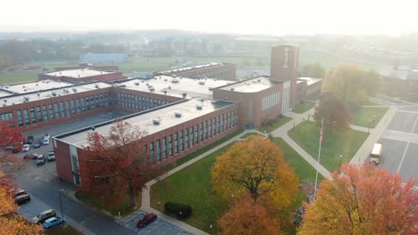 high angle aerial of school bus leaving large public school on foggy morning