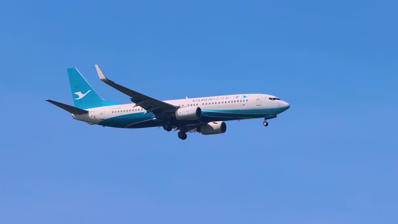 A commercial jet aircraft glides smoothly through a clear blue sky, showcasing its aerodynamic design and landing gear.
