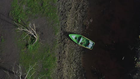 Captured-from-Above:-Drone-Exposes-a-Fishing-Boat-Resting-on-the-Shoreline,-Creating-a-Vivid-Contrast-of-Blue-and-Green-Amidst-Scattered-Fallen-Woods