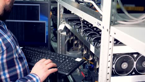 male specialist is setting necessary parameters with a keyboard while graphic cards are mining