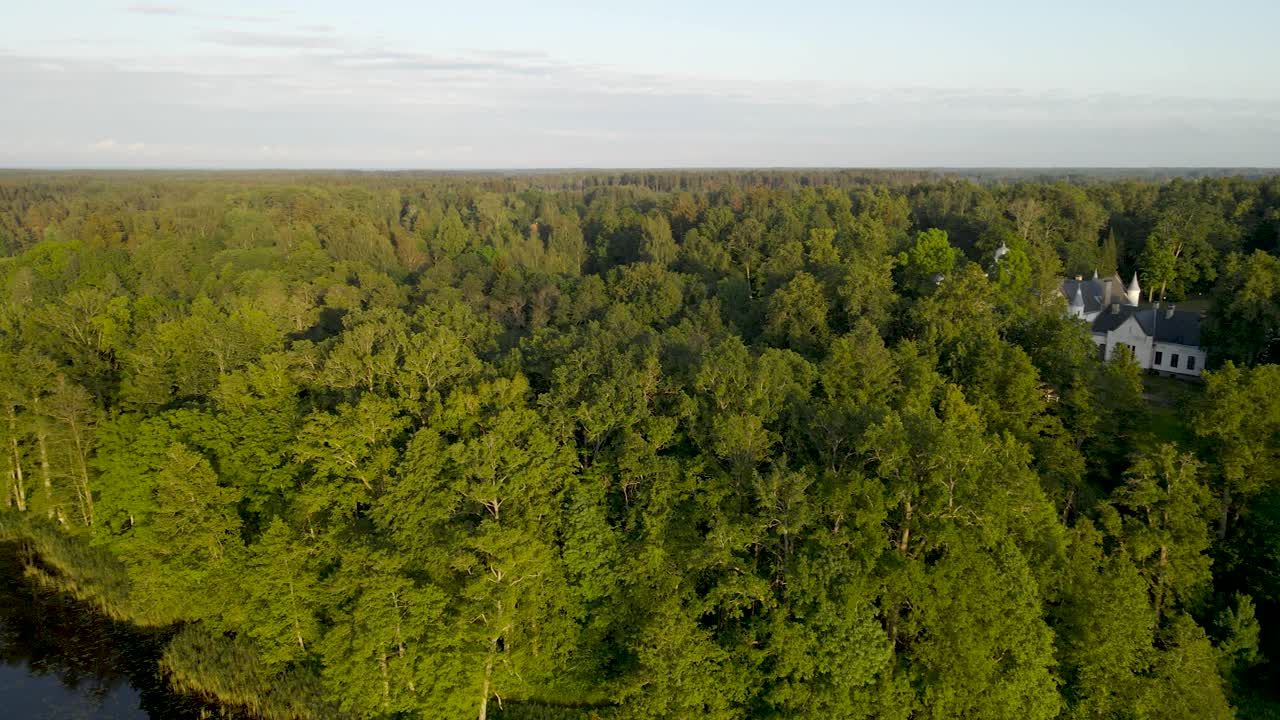 Aerial drone footage panning above a large dark colored reflective Alatskivi lake during sunset that has a white small bridge going over it and a large historic medieval white castle and turrets seen