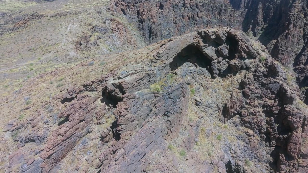 Ripresa aerea ravvicinata verso il famoso arco naturale di Coronadero, che mostra strati di roccia viola e grigia inclinati sulla cresta sopra il canyon di Barranco Hondo