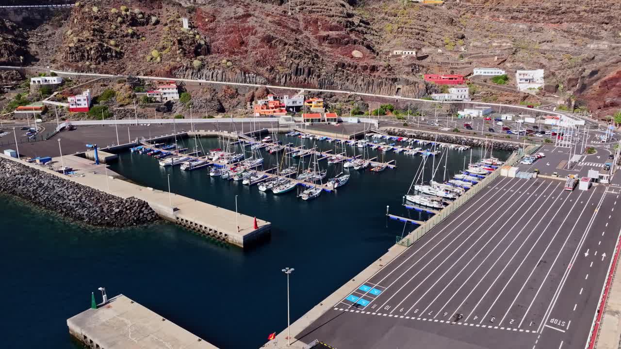 Establishing aerial of Puerto de la Estaca harbor with boats and rocky coastline