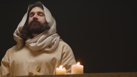 shot of man wearing robes with long hair and beard representing figure of jesus christ holding wooden cross