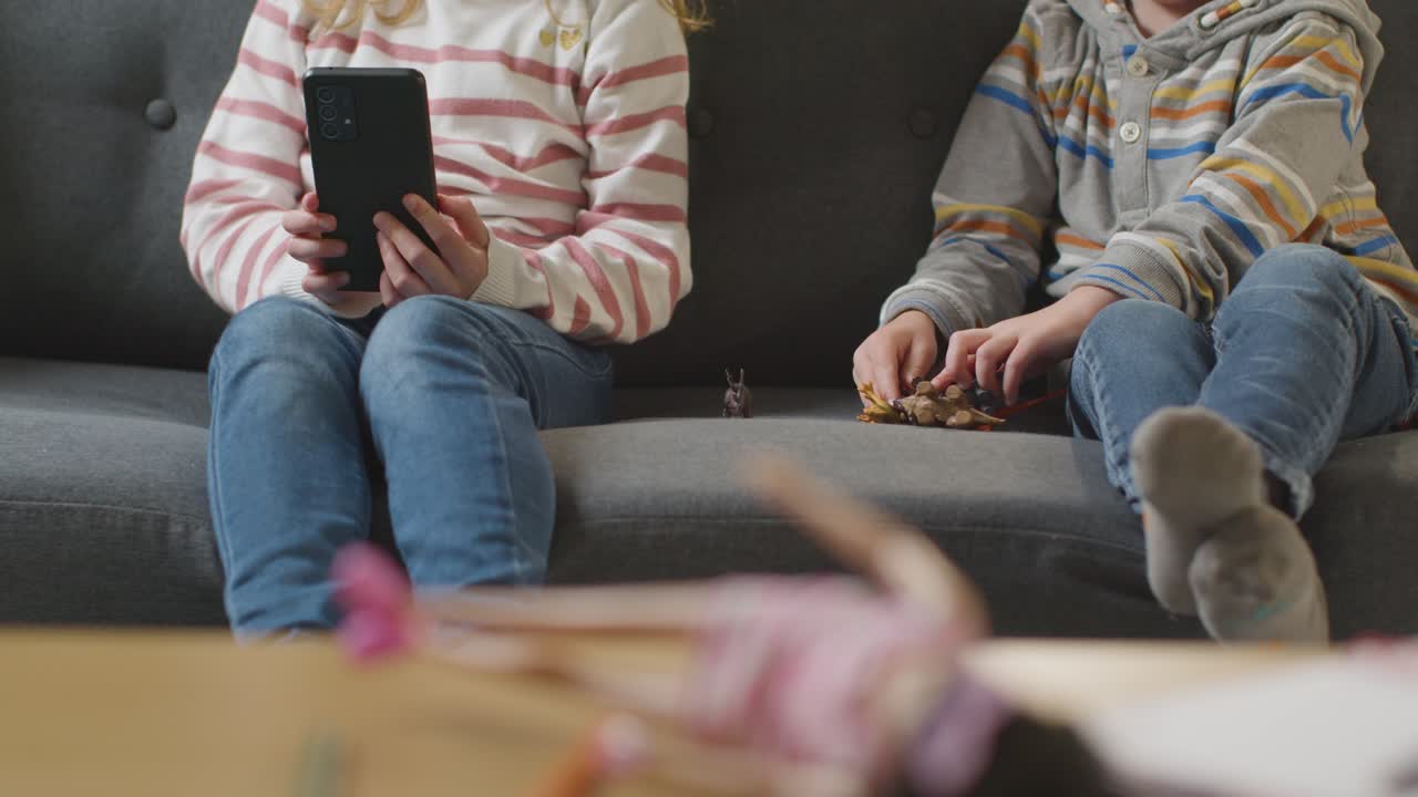 소년 이 장난감 공 ⁇  과 함께 놀면서 소녀 가  ⁇ 드폰 을 사용 하고 있는 모습