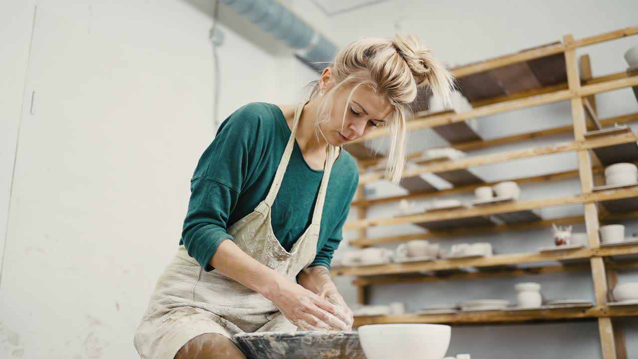 Female potter sitting at pottery workshop and making ceramic pot on wheel, below view, slow motion