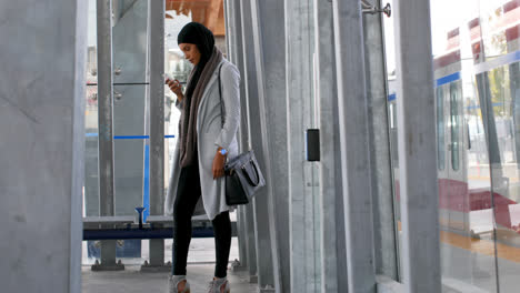 side view of young asian woman in hijab using mobile phone at railway station 4k